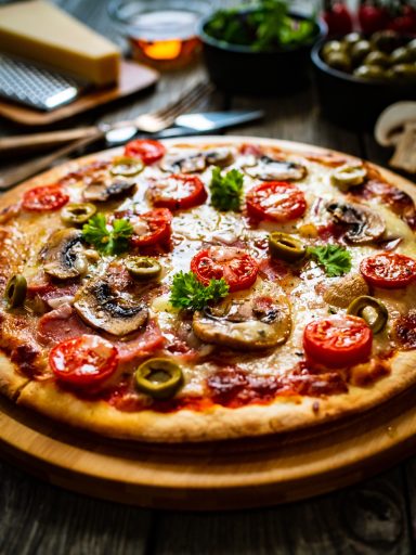 Pizza Pizza mit Tomaten, Pilzen, Oliven und frischen Kräutern auf einem Holzbrett.
