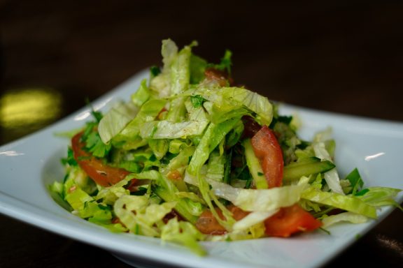 Salat Frischer Salat mit grünen Blättern, Tomaten und Kräutern in einer weißen Schüssel.