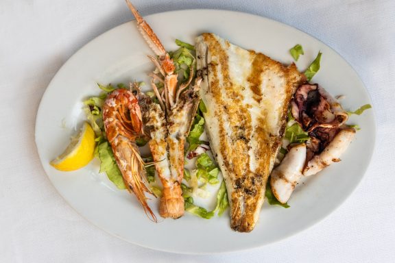 Fisch Gegrillter Fisch mit Garnelen, Tintenfisch und einem Zitronenschnitz auf Salat.